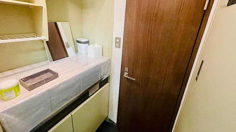 更衣室の様子。台の上には綿棒やティッシュなどのアメニティ、鏡や小さめのごみ箱が設置されている。トイレにつながる扉がある。