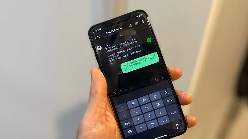 スマートフォンを操作し、LINEで「明日の16時から90分セルフトレーニングで予約を取りたいです」というメッセージをジムのアカウントに送信している画面」