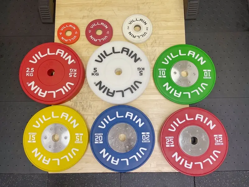 床に並べられた、TAKASE GYM で扱う全種類のバーベルプレート。VILLAIN製の多様な重量のカラフルなプレートが並んでいる。