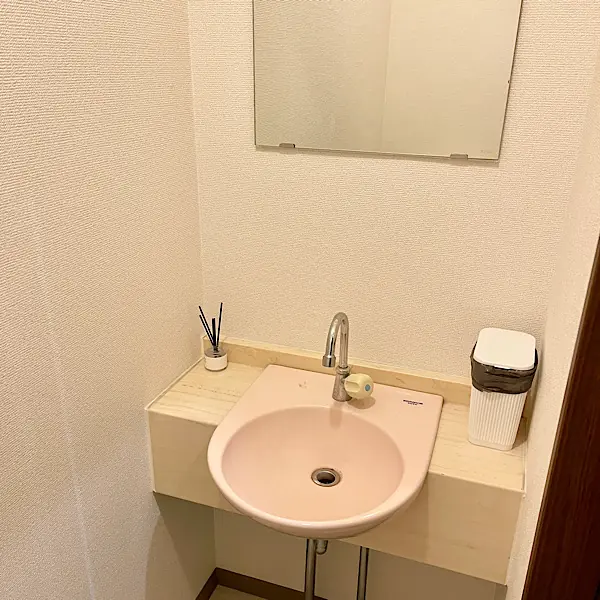 トイレ内の手洗いスペース。鏡、ピンク色の洗面ボウル、アロマディフューザーが設置された清潔感のある空間。