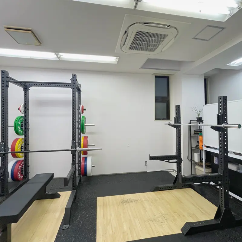 本格的なハーフラックと重量別のカラープレート、トレーニングベンチ、予備のスクワットスタンドが整然と並ぶTAKASE GYMの内観